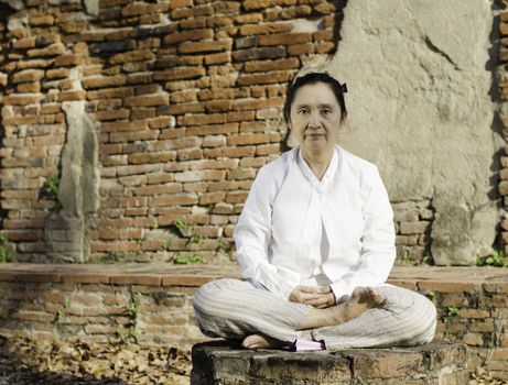 Buddhist woman meditating against ancient temple