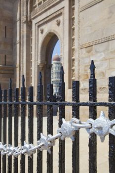 Vertical take of the Gateway of India, its black and silver painted railings with a defocused cameo view of the Taj Hotel from an angled view of an archway