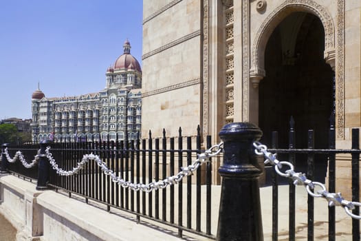 Landscape of the Gateway of India, its black and silver painted railings with a cameo view of the Taj Hotel with an angled view of an archway