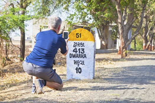 Rural landscape in Gujarat India on the route to Dwarka a holy city for Hindus and Mahabharata, caucasian male taking a photo of the 413km milestone to Dwarka passing through Mahuva