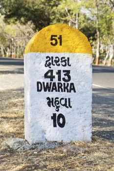 Portrait landscape in rural Gujarat India incorporating 413 kilometers to Dwarka milestone and land mark on the coastal road to Dwarka the religious town for Hindus