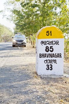 Rural landscape in Gujarat India incorporating 85 kilometers to Bhavnagar milestone and land mark on the coastal road to Dwarka a religious town for Hindus. Parked people carrier with head lights switched on