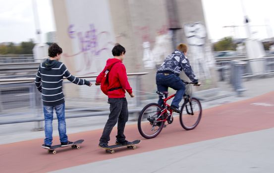 Teenagers riding bikes and skateboards on urban bicycle trail.