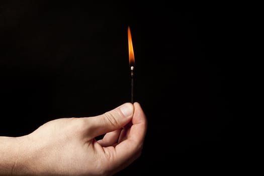 Hand holding burning match stick on black background