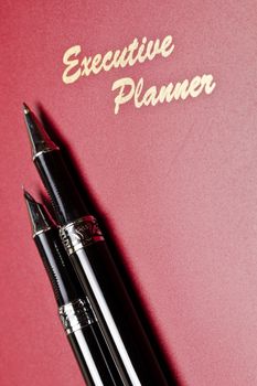 angled view of a red executive planner with slanting pens and wording