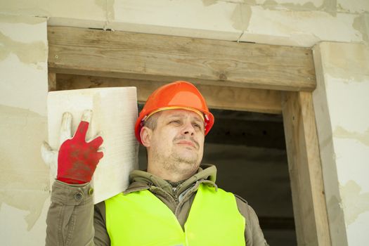 Builder with a concrete block on shoulder at new building