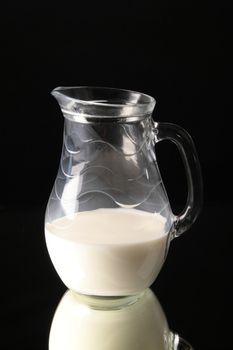 Glass jug with milk on black background