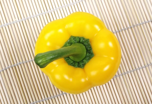 Yellow bell pepper with green stem laying on asian wooden mat.