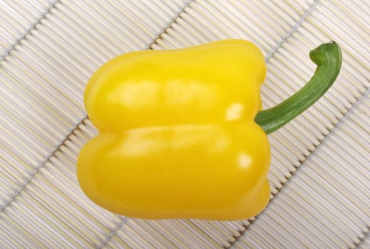 Yellow bell pepper laying on wooden asian mat. Studio shot.