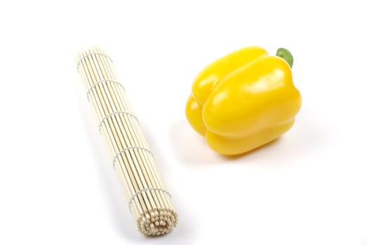 Yellow pepper and rolled japanese mat isolated on white background with shadow.