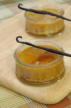 Creme caramel dessert served in glass ramekins and decorated with vanilla pods