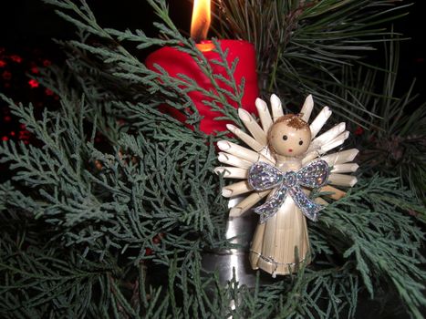 christmas arrangement with a small angel surroundet by fir spruces and a red candle