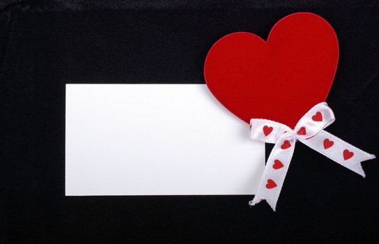 White card with red heart isolated on black velvet background. Empty space for your design.