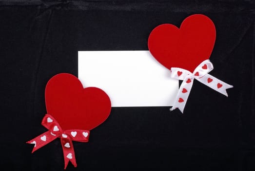 Two red hearts and white card isolated on black velvet background. Empty space for your design.