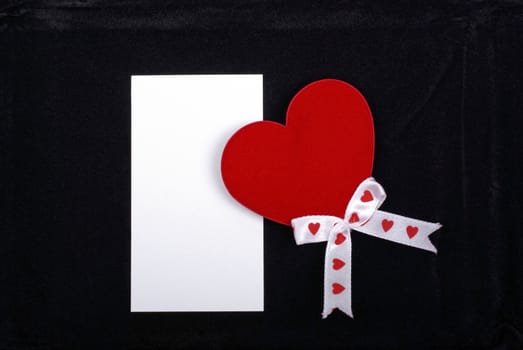 Red heart with white ribbons and empty card isolated on black velvet background.
