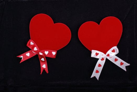 Two hearts with ribbons isolated on black velvet background.