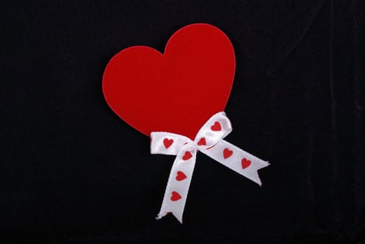 Red heart with white ribbons isolated on black velvet background.