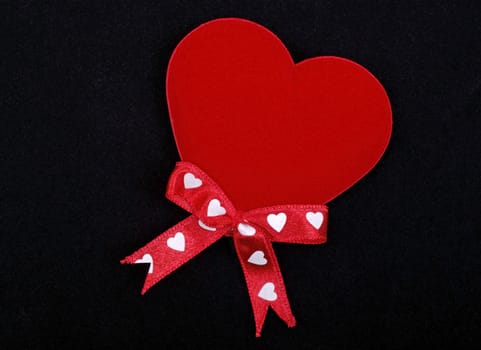 Macro of red heart with ribbons isolated on black velvet background.