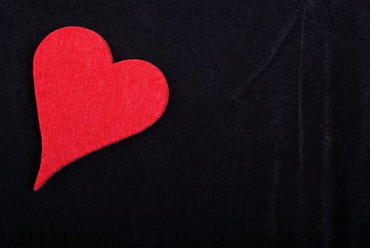 Red heart isolated on black velvet textured background. Empty space for your design.