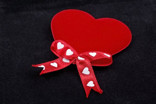 Red heart with silk ribbons macro isolated on black velvet background.