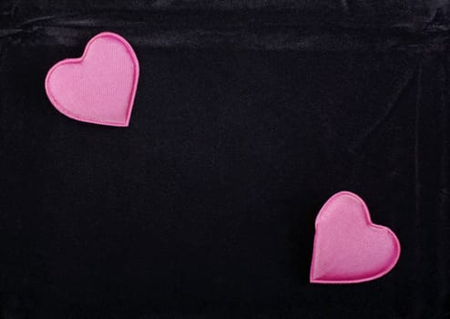 Two pink hearts isolated on black velvet background. Empty space for your design.