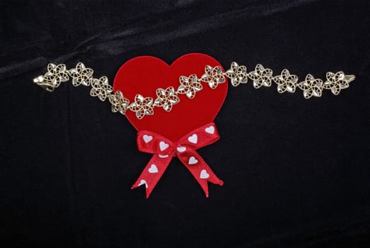 Golden bracelet with red heart isolated on black velvet background.