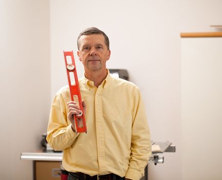 Senior male in a home workshop facing the camera and holding a level