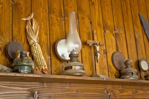 Old lantern, crucifixion, corncob and paraffin lamp on shelf, with wooden background