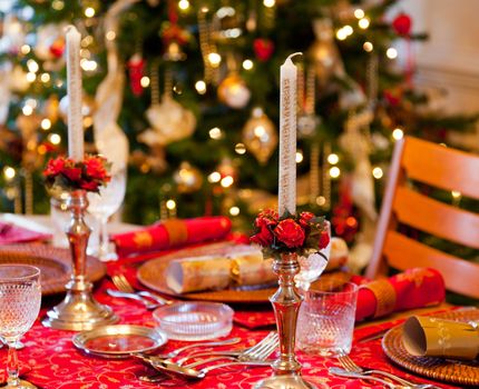 Christmas crackers on table set for Christmas lunch with candles and tree in background