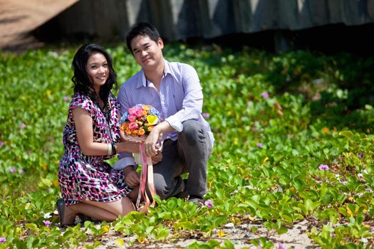 attractive young couple sitting on beach grass meadow  with flower bouquet