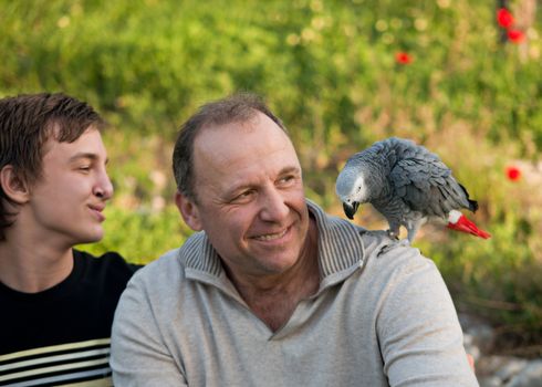 Portrait of a boy teenager and his father with a gray parrot Jaco.