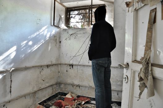 Hooded man looking through the broeken window of abandoned house.