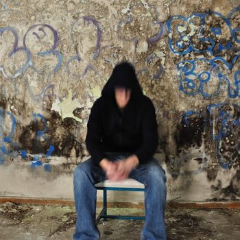 Blurry male figure sitting against dirty wall covered with black mold and messy paint.