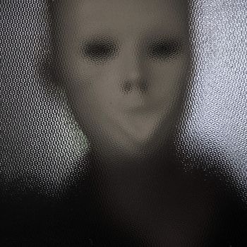 Masked distorted figure behind stained glass surface.