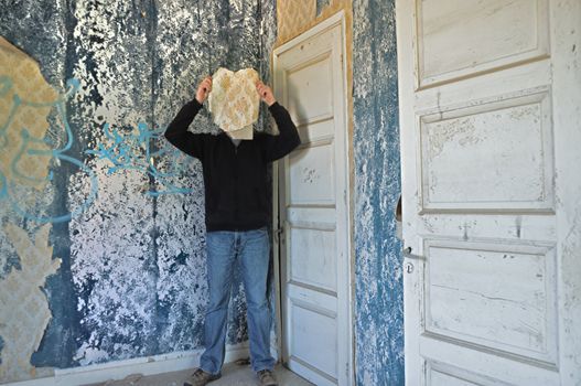 Male figure obscured by torn wallpaper shred in abandoned house interior.