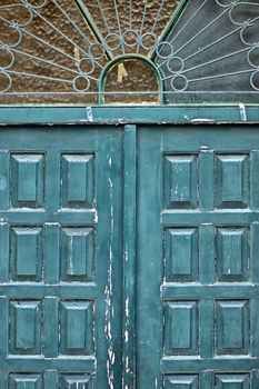 Weathered blue wooden gate with vintage ornamental sun pattern metalwork.