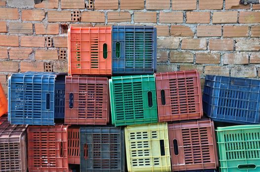 Plastic crates and brick wall background. Pile of colorful fruit packing containers.
