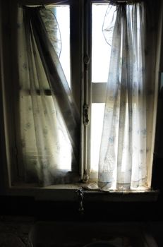 Window curtains and dirty kitchen sink in abandoned house.