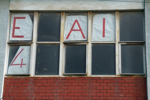 Forgotten crumbling for rent sign on dusty windows of abandoned building.