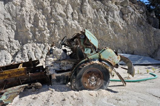 Rusty vintage car and discarded machinery half buried in the sand at gravel quarry.