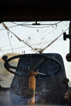 Steering wheel and driver cabin of industrial machinery. Light reflections on broken windscreen glass.