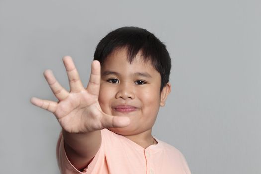 Child looking at camera. Stop signal with his hand. over gray background 
