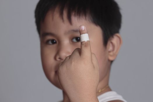 boy with a bandaged finger on gray background 
