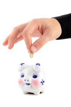 Hand inserting coin into piggy-bank isolated on white