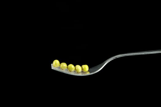 Fresh green peas on a silver fork, over black background.