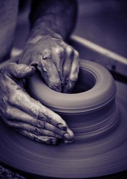 Hands working on pottery wheel , close up retro style toned photo wit shallow DOF