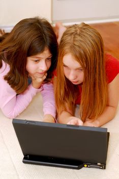 Portrait of two girls lying on the floor and  looking into computer