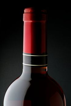 Red wine bottle closeup with red capsule and black background
