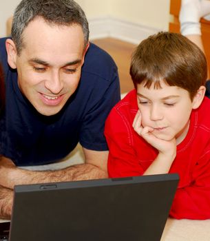 Father and son lying on the floor at home and looking into a portable computer