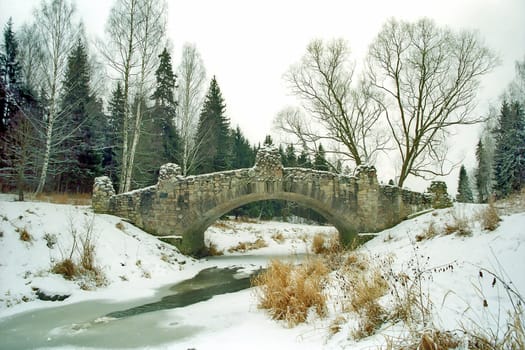 Ancient stone bridge over iced river in park